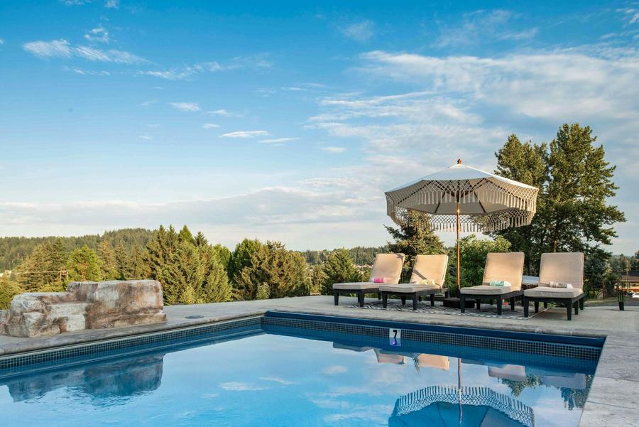 Lounge chairs under a fringed umbrella beside the pool, with a forested valley view